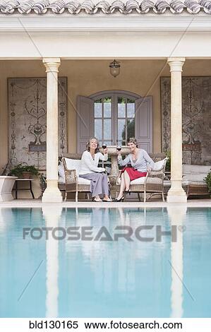 Stock Photography - Women toasting each other by swimming pool. Fotosearch