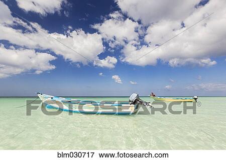 Stock Photo - Boats tied to tropical beach under blue sky. Fotosearch