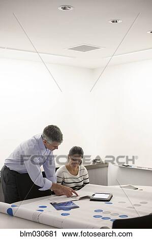 Stock Image - Business people examining blueprints in meeting. Fotosearch