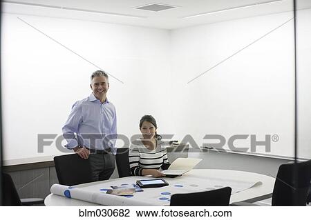 Stock Image - Business people examining blueprints in meeting. Fotosearch