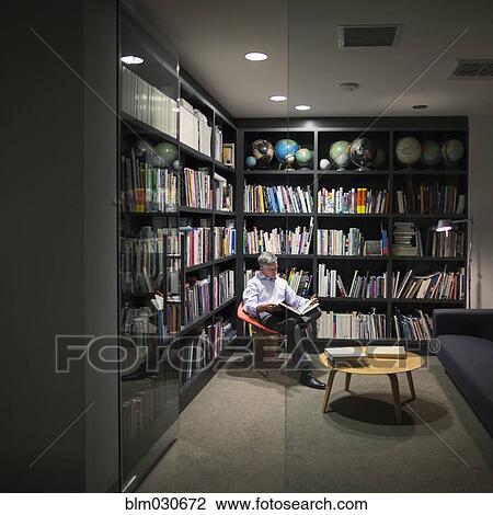 Stock Image - Caucasian businessman reading in library. Fotosearch