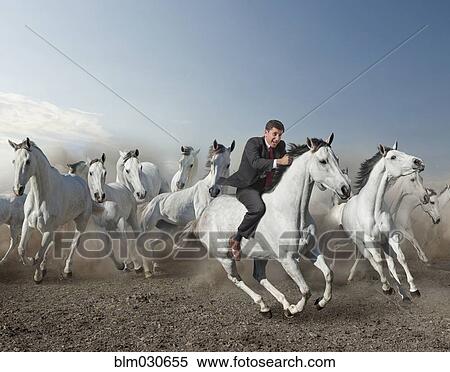 Stock Photography - Caucasian businessman riding wild horse in desert. Fotosearch