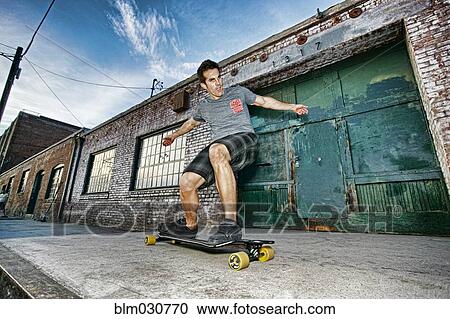 Caucasian man riding skateboard on city street View Large Photo Image Stock Image - Caucasian man riding skateboard on city street. Fotosearch