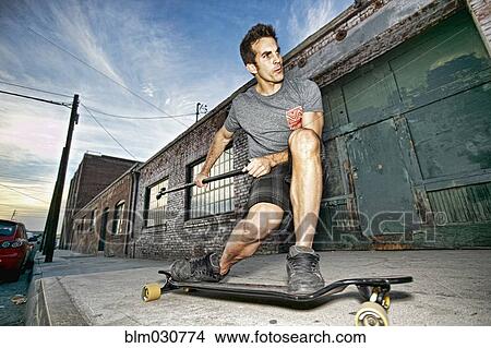 Picture - Caucasian man riding skateboard with land paddle. Fotosearch
