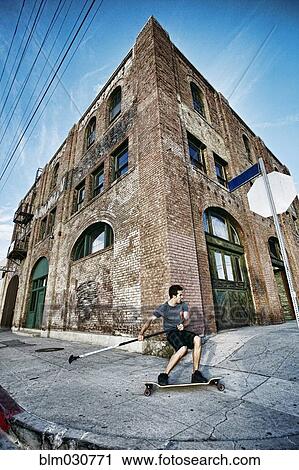 Stock Image - Caucasian man riding skateboard with land paddle. Fotosearch
