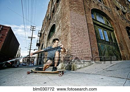 Stock Image - Caucasian man riding skateboard with land paddle. Fotosearch