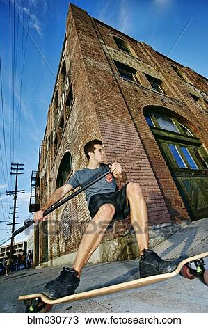 Stock Image - Caucasian man riding skateboard with land paddle. Fotosearch