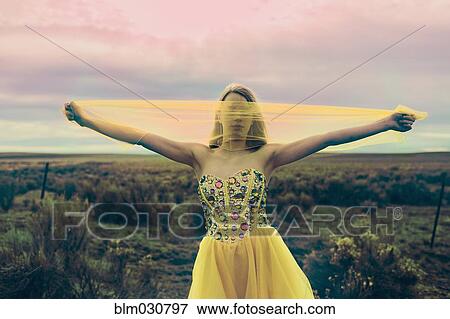 Stock Photo - Caucasian teenage girl playing with scarf in rural field. Fotosearch