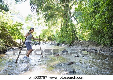 Stock Photo - Hispanic woman crossing jungle stream. Fotosearch