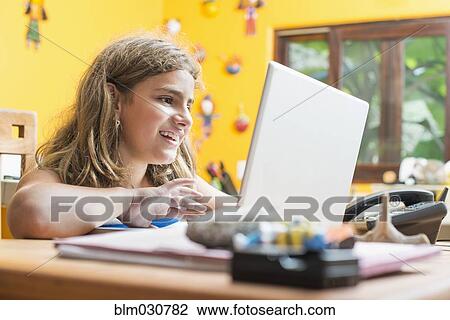 Stock Image - Mixed race girl using laptop at desk. Fotosearch