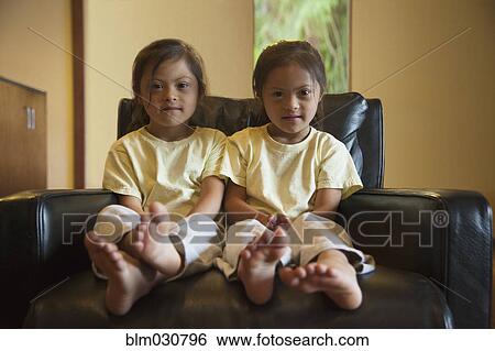 Stock Photograph - Mixed race twins with Down syndrome sitting in armchair. Fotosearch