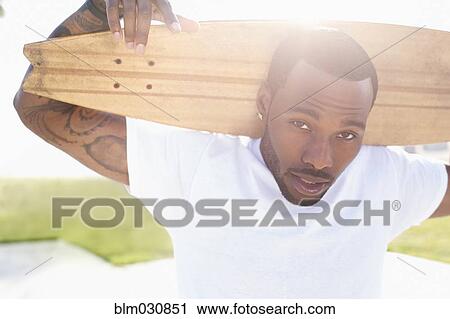 Stock Image - African American man carrying skateboard outdoors. Fotosearch