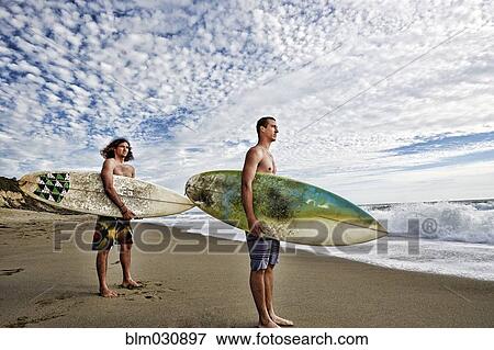 Stock Photo - Caucasian men carrying surfboards on beach. Fotosearch