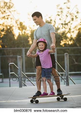Stock Photograph - Father and daughter riding skateboard in park. Fotosearch