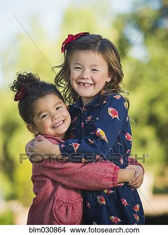 Picture - Mixed race girls hugging outdoors. Fotosearch