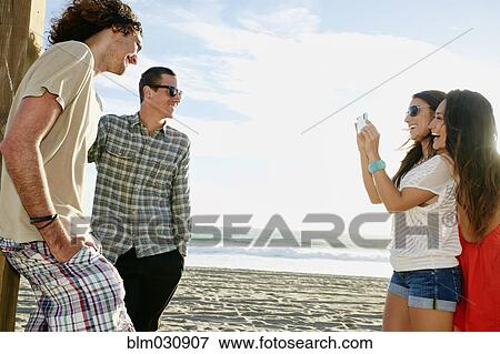 Stock Photo - Women taking picture of boyfriends on beach. Fotosearch