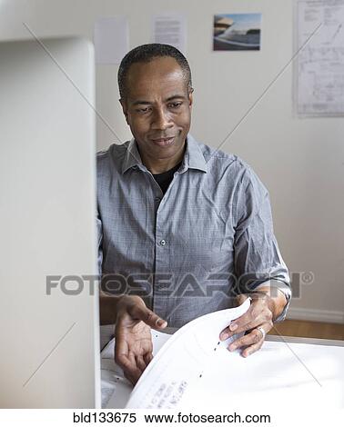 Stock Photography - African American architect examining blueprints in office. Fotosearch