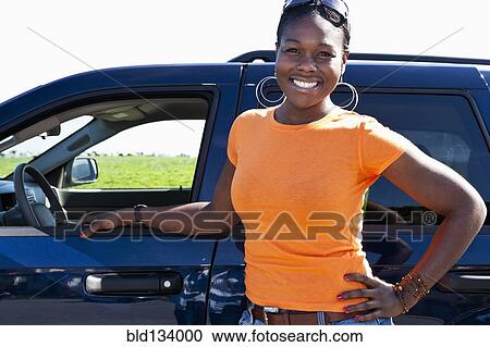 Stock Image - African American woman standing by car. Fotosearch