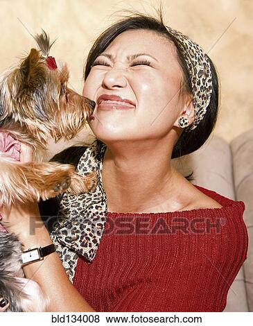Stock Photo - Asian woman holding dog on sofa. Fotosearch