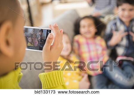 Stock Image - Boy photographing friends on sofa. Fotosearch