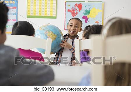 Stock Image - Boy showing globe to classroom. Fotosearch