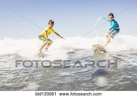 Stock Image - Boys surfing in ocean. Fotosearch