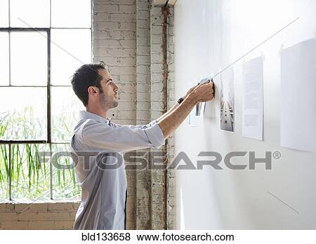Stock Photo - Caucasian architect hanging photos in office. Fotosearch