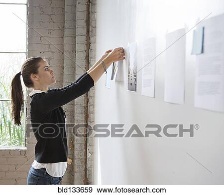Stock Photo - Caucasian architect hanging photos in office. Fotosearch