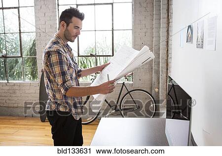Stock Image - Caucasian architect reading blueprints in office. Fotosearch