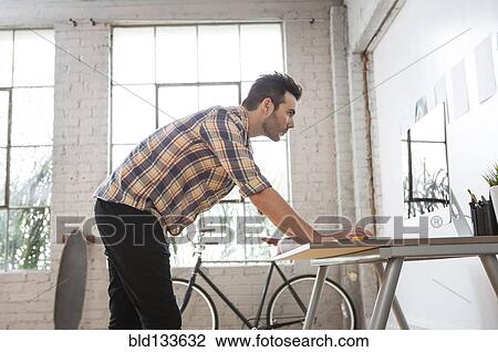 Stock Image - Caucasian architect reading blueprints in office. Fotosearch