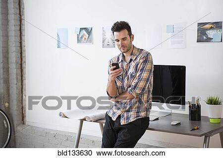 Stock Image - Caucasian architect using cell phone in office. Fotosearch