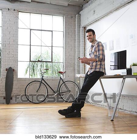 Stock Photo - Caucasian architect using cell phone in office. Fotosearch
