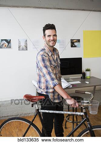 Stock Photography - Caucasian architect wheeling bicycle in office. Fotosearch
