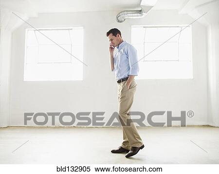 Stock Photography - Caucasian businessman talking on cell phone in empty office. Fotosearch