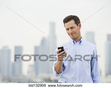 Stock Photo - Caucasian businessman using cell phone on urban rooftop. Fotosearch