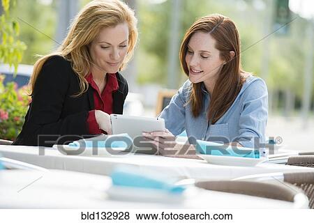 Stock Photo - Caucasian businesswomen using digital tablet at lunch. Fotosearch