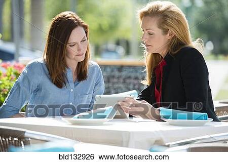 Stock Photograph - Caucasian businesswomen using digital tablet at lunch. Fotosearch