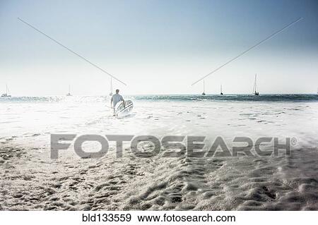 Stock Photo - Caucasian man carrying surfboard into ocean. Fotosearch