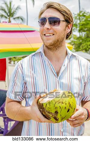 Caucasian man drinking from coconut on beach View Large Photo Image Stock Photograph - Caucasian man drinking from coconut on beach. Fotosearch