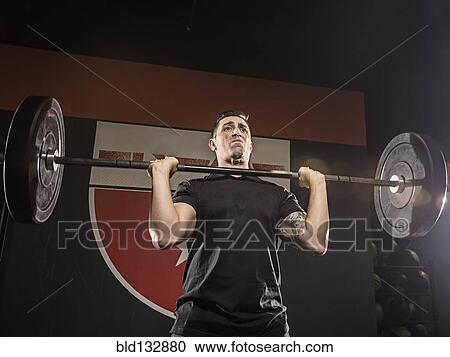 Stock Image - Caucasian man lifting weights in gym. Fotosearch