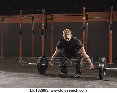 Stock Image - Caucasian man lifting weights in gym. Fotosearch