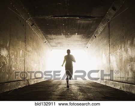 Stock Image - Caucasian man running in urban tunnel. Fotosearch