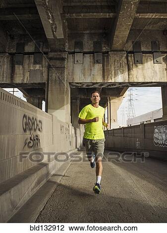 Stock Image - Caucasian man running in urban tunnel. Fotosearch