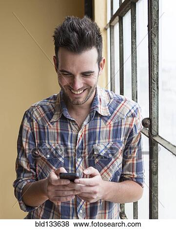 Stock Photo - Caucasian man using cell phone by window. Fotosearch