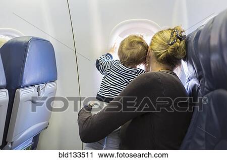 Stock Image - Caucasian mother and baby looking out airplane window. Fotosearch