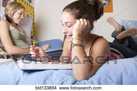 Picture - Caucasian teenage girls doing homework on bed. Fotosearch