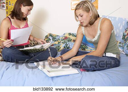Stock Image - Caucasian teenage girls doing homework on bed. Fotosearch
