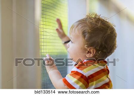 Picture - Caucasian toddler peering out screen door. Fotosearch
