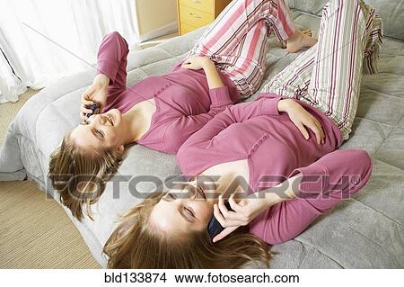 Picture - Caucasian twin teenage girls talking on cell phones. Fotosearch