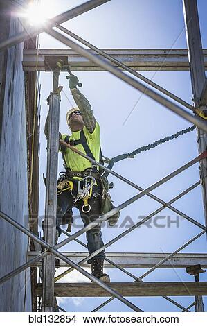 Picture - Caucasian worker on scaffolding on construction site. Fotosearch